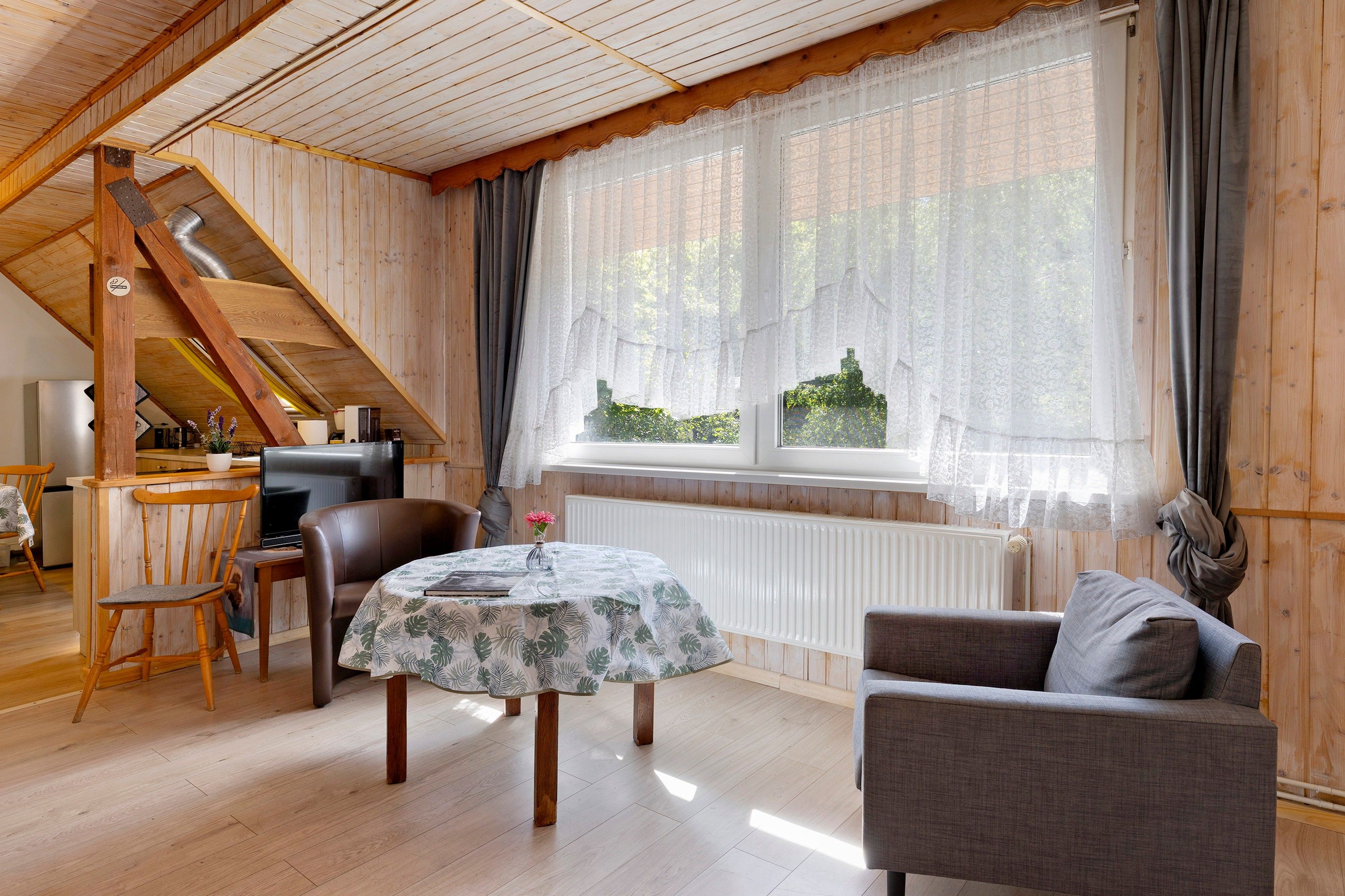 A cozy room with a wooden ceiling, a dining table with chairs, a sofa, and a large window with curtains.