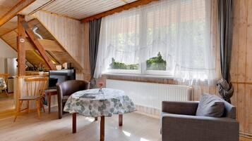 A cozy room with a wooden ceiling, a dining table with chairs, a sofa, and a large window with curtains.