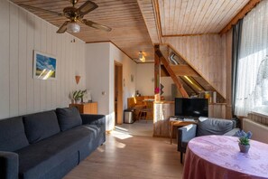A cozy living room with a sofa, a table, a TV, and a staircase leading to another level.
