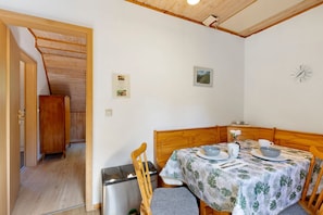 A dining area with a wooden table set for two, a clock on the wall, and a small framed picture.