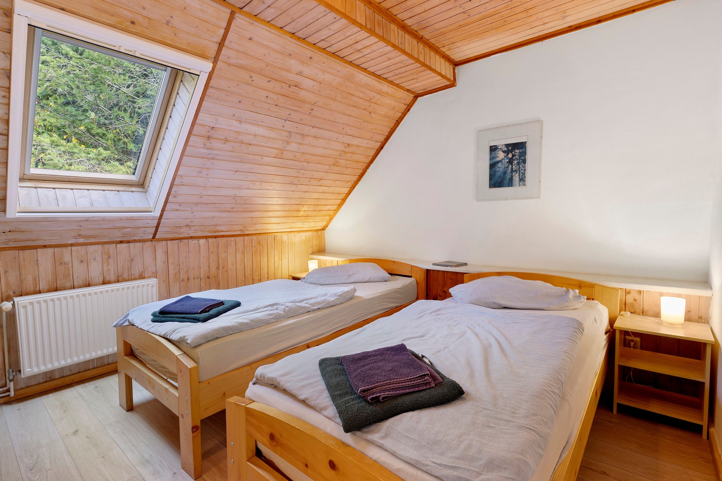 Une petite pièce chaleureuse, avec deux lits en bois, une fenêtre et un radiateur.