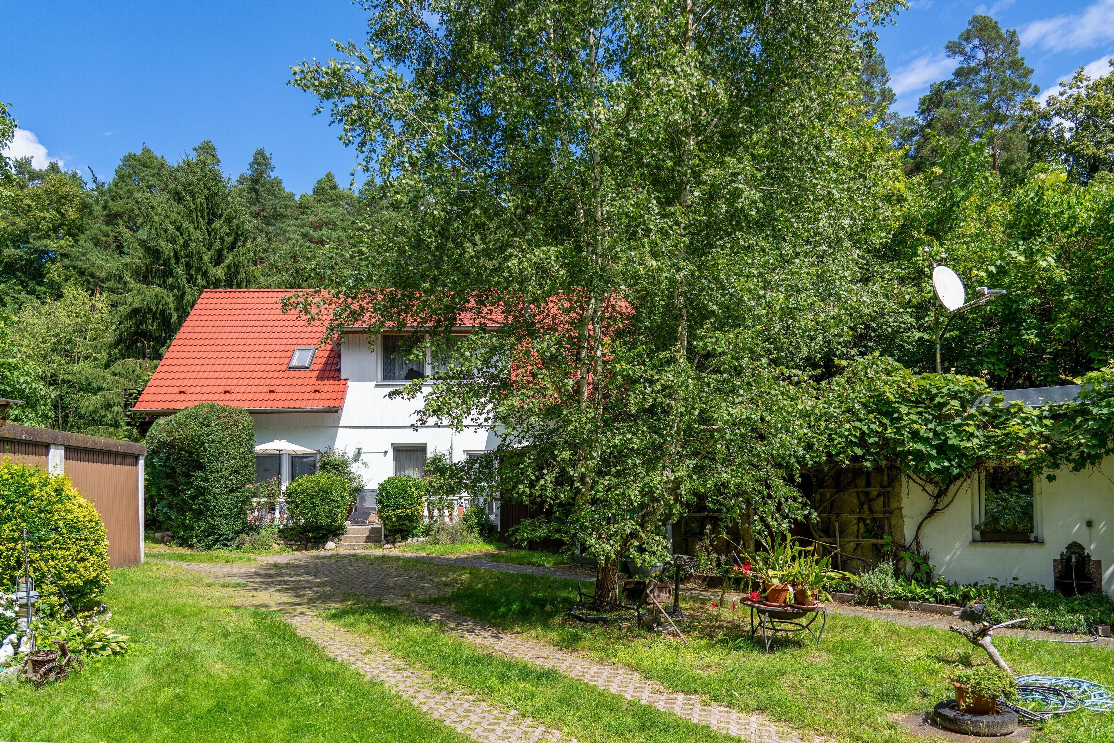 Ein Haus mit rotem Dach, umgeben von üppigem Grün und einem gepflasterten Weg.