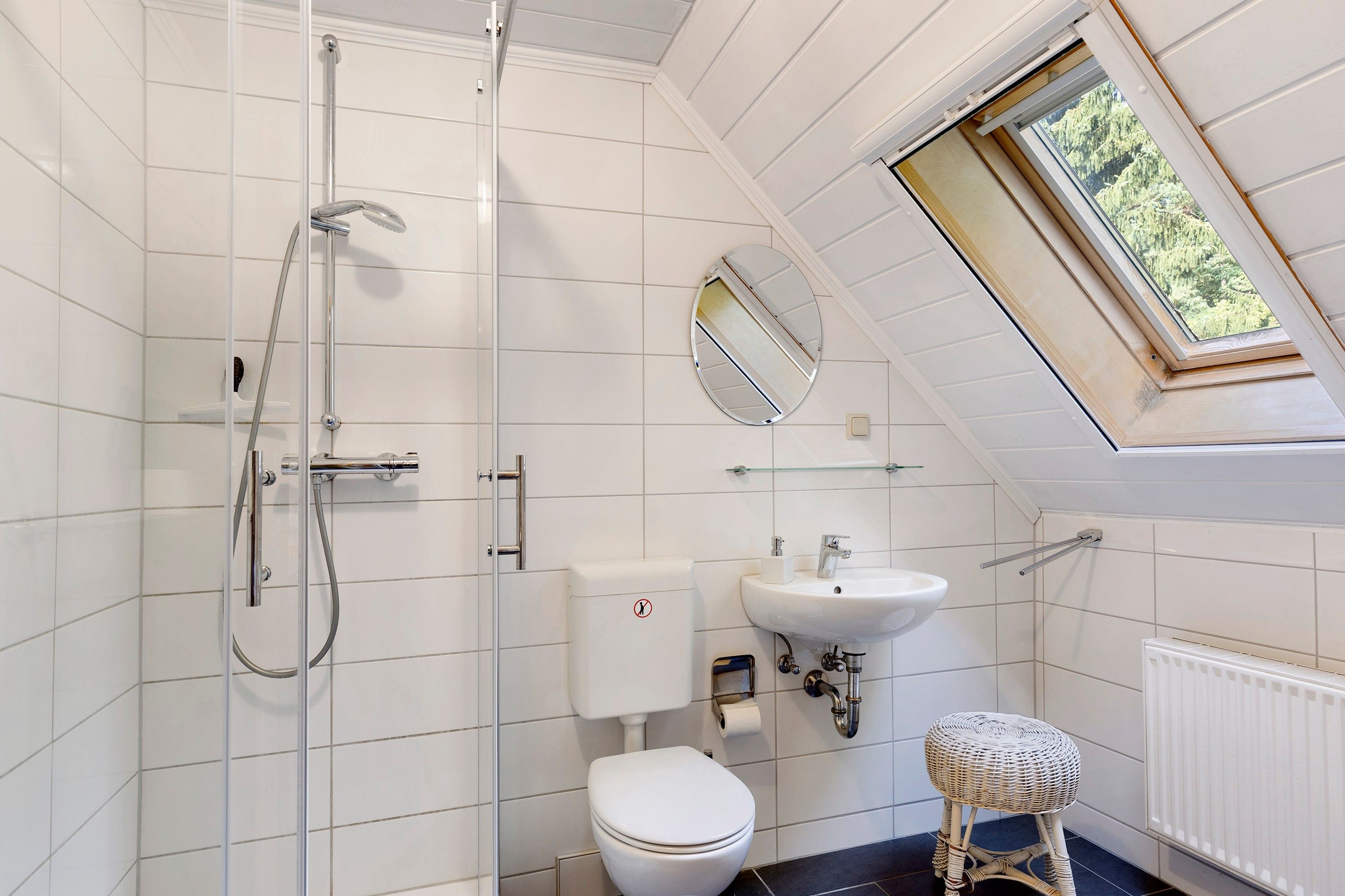 Een badkamer met douche, toilet, wastafel en een raam.