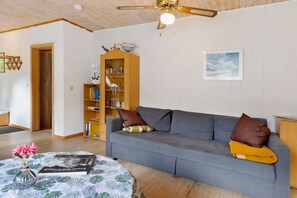 A living room with a grey sofa, a wooden bookshelf, a ceiling fan, and a framed picture on the wall.