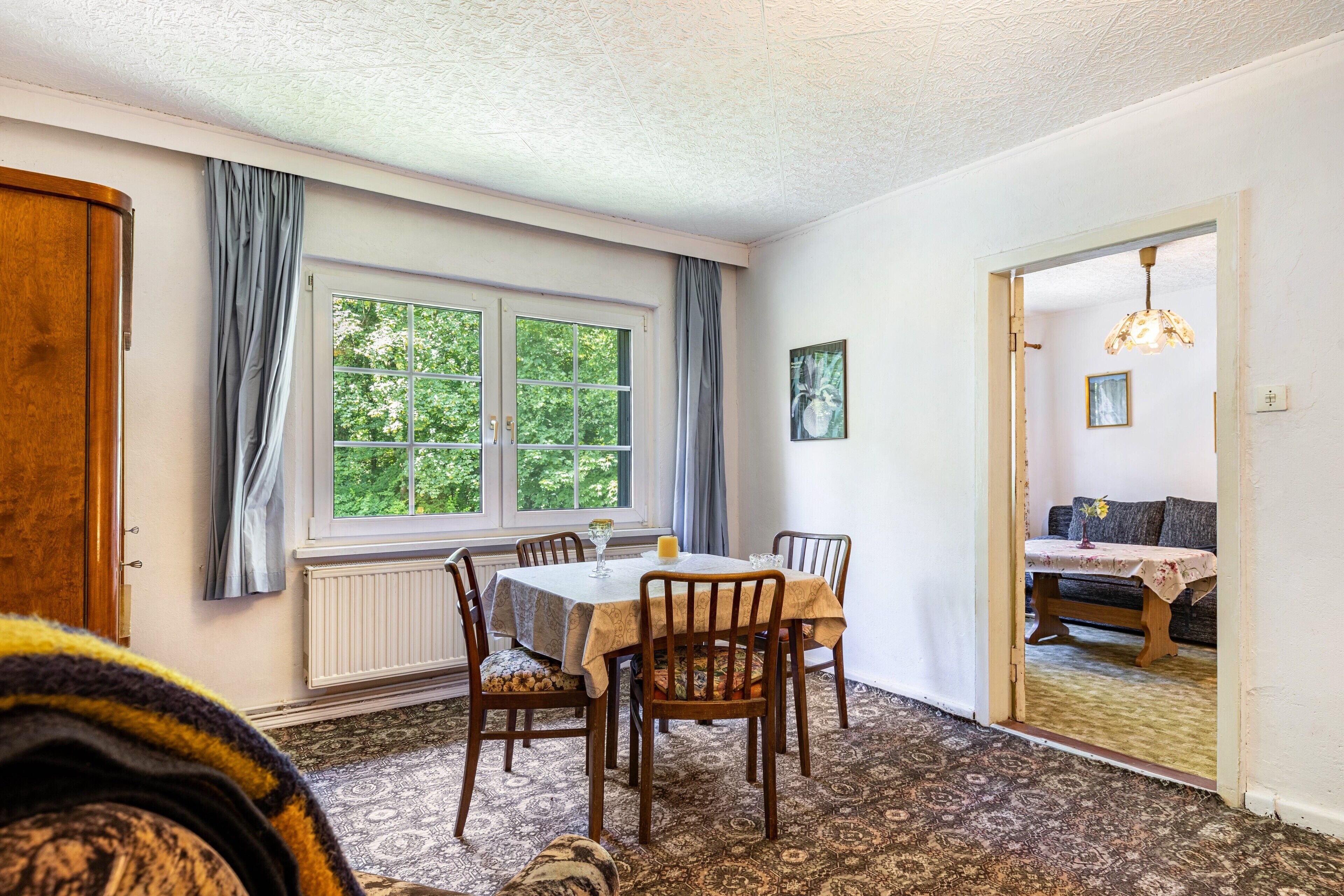 A dining area with a table, chairs, a window with curtains, a radiator, and a patterned carpet.
