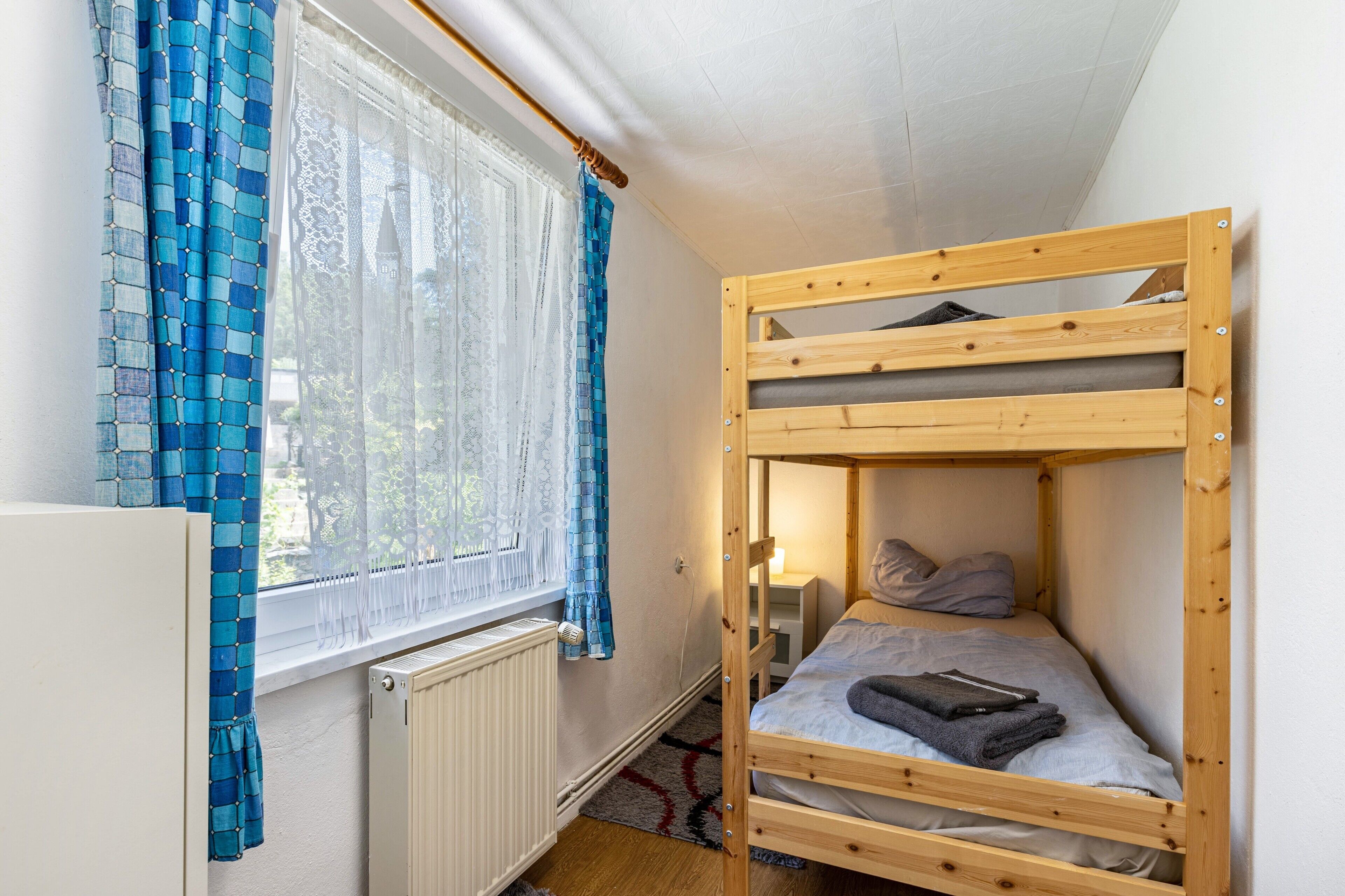 Et soveværelse med køjeseng, et vindue, gardiner og en radiator.