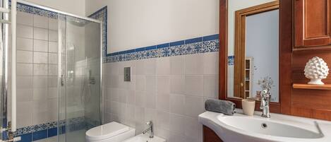 A bathroom with a glass shower enclosure, a bidet, and a sink with a mirror.
