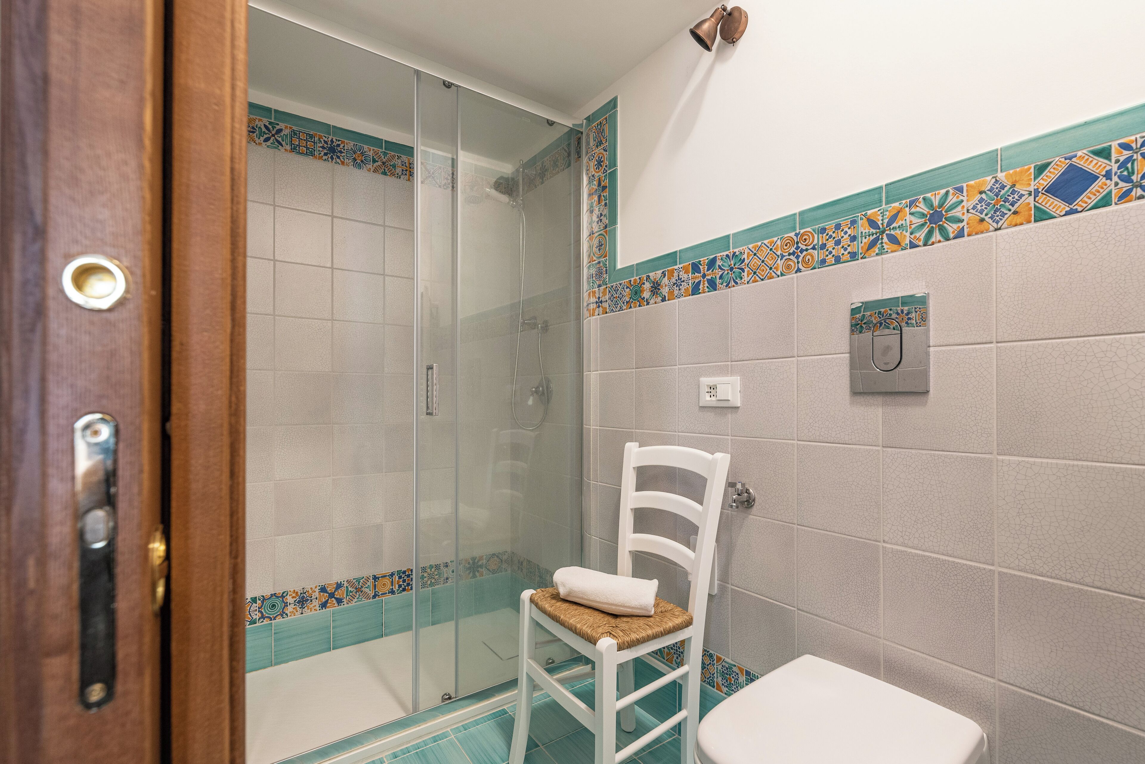 Une salle de bain avec une douche à parois de verre, des toilettes blanches et une chaise sur laquelle est posée une serviette.
