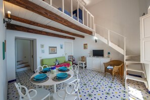 A dining area with a white table set for four, a green sofa, and a staircase leading to a loft.