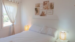 Ett sovrum med en säng, två sänglampor, ett fönster med gardin och konst på väggen.
