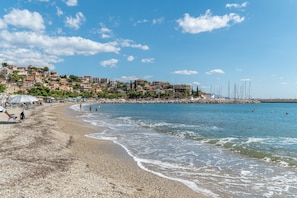 Une plage de galets, un ciel dégagé et des bâtiments en arrière-plan.
