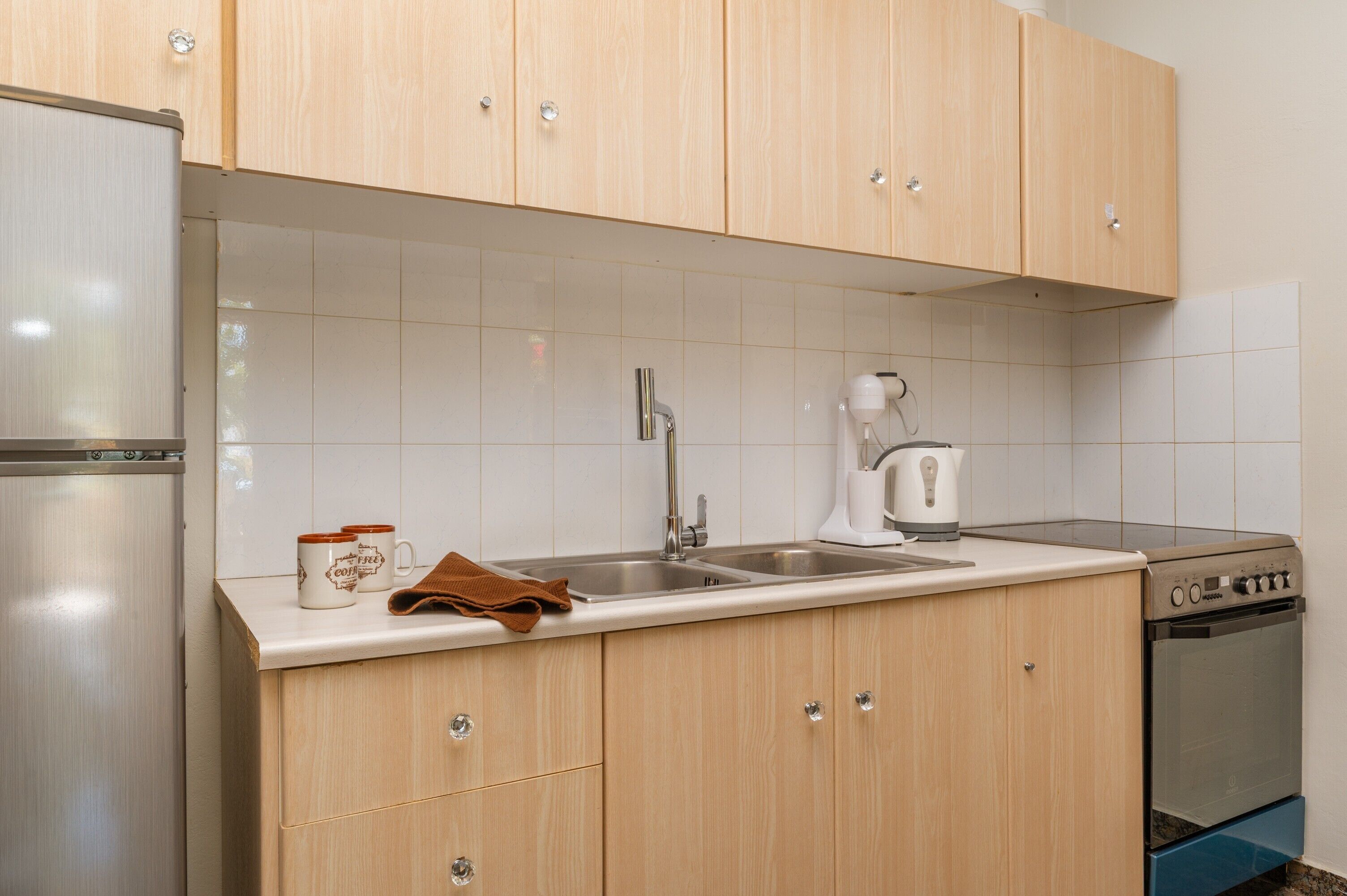 A kitchen with wooden cabinets, a stainless steel sink, a kettle, and a dishwasher.