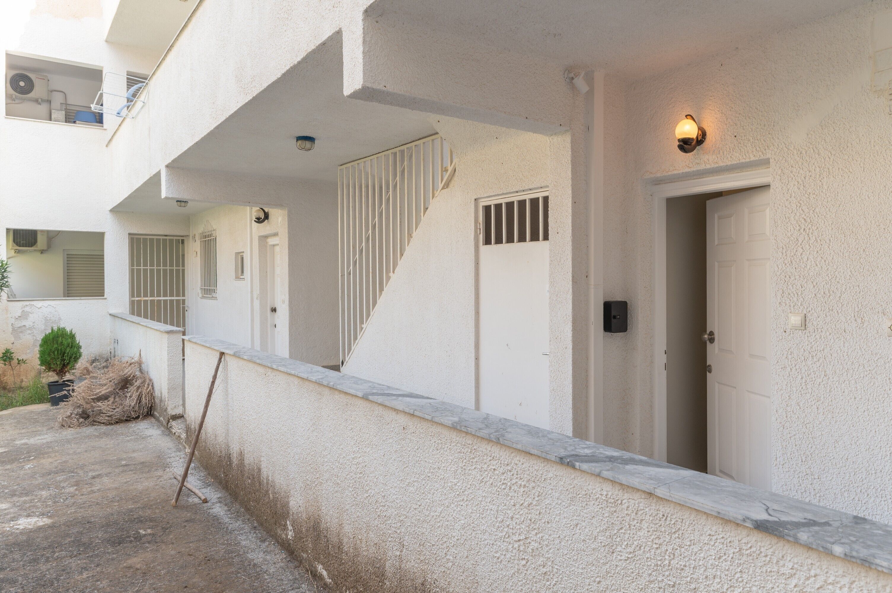 Un edificio con facciata bianca, una porta, una finestra con sbarre, una piccola pianta in vaso e una telecamera di sicurezza.