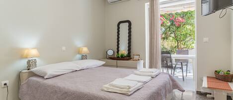 A bedroom with a bed, bedside lamps, a mirror, a TV, and a view of the outdoors.