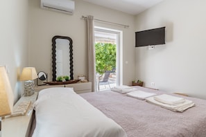 Une chambre d’hôtel avec un lit, une télévision, une fenêtre avec des rideaux, un miroir et une petite table avec une lampe.