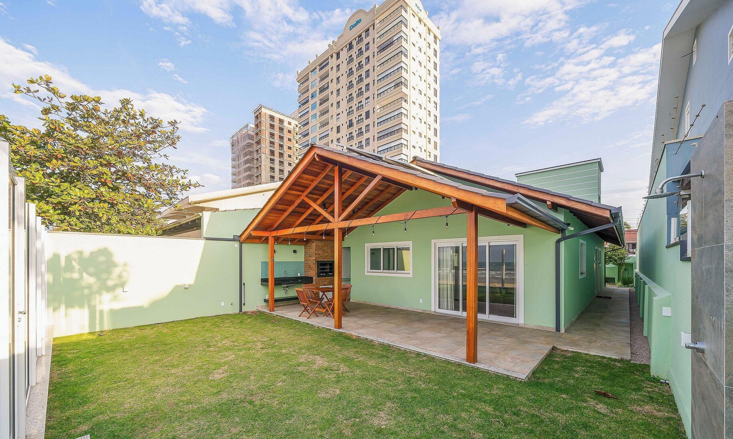 A residential building with a covered patio, a small lawn, and a tall building in the background.