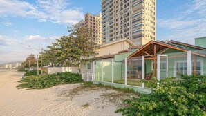 Ein Küsteneigentum mit einer verglasten Terrasse, einem Sandstrand und Hochhäusern im Hintergrund.