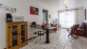 A dining area with a wooden cabinet, a table with chairs, a microwave, and a painting on the wall. - Apt w Barbecue 350m fr Canasvieiras Beach Aal0204 (Florianópolis)