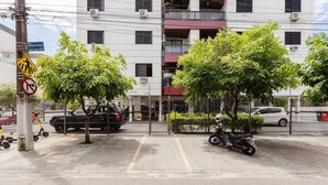 A gated parking area with a motorcycle, trees, and a multi-story building in the background. - Apt w Barbecue 350m fr Canasvieiras Beach Aal0204 (Florianópolis)