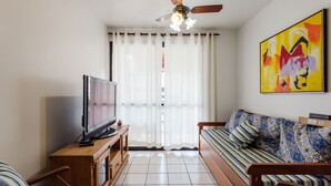 A living room with a TV on a wooden stand, a ceiling fan, a sofa with patterned cushions, and a large abstract painting on the wall. - Apt w Barbecue 350m fr Canasvieiras Beach Aal0204 (Florianópolis)