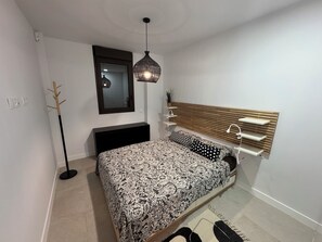Un dormitorio moderno con una cama, estantes a los lados, una lámpara colgante y un perchero.
