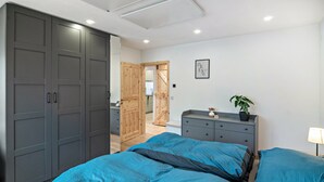 Un dormitorio con un armario grande, una cama con ropa de cama azul, un tocador y una mesita de noche con una lámpara.