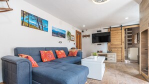 A modern living room with a sectional sofa, a flat-screen TV, and a sliding door leading to a kitchen.