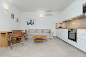 Une cuisine moderne avec des armoires blanches, un four encastré et un coin repas comprenant une table et des chaises en bois.
