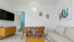 Una sala moderna con televisor de pantalla plana, una mesa de comedor de madera y sillas, un sofá y un cuadro de veleros en la pared.