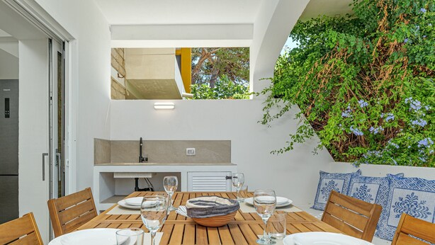 Un comedor con una mesa de madera preparada para cuatro personas, una cocina integrada y vistas a un jardín.