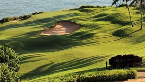 Een golfbaan met een waterpartij en bergen op de achtergrond.
