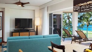 Een hotelkamer met een bank, stoelen, een televisie en een balkon met stoelen.