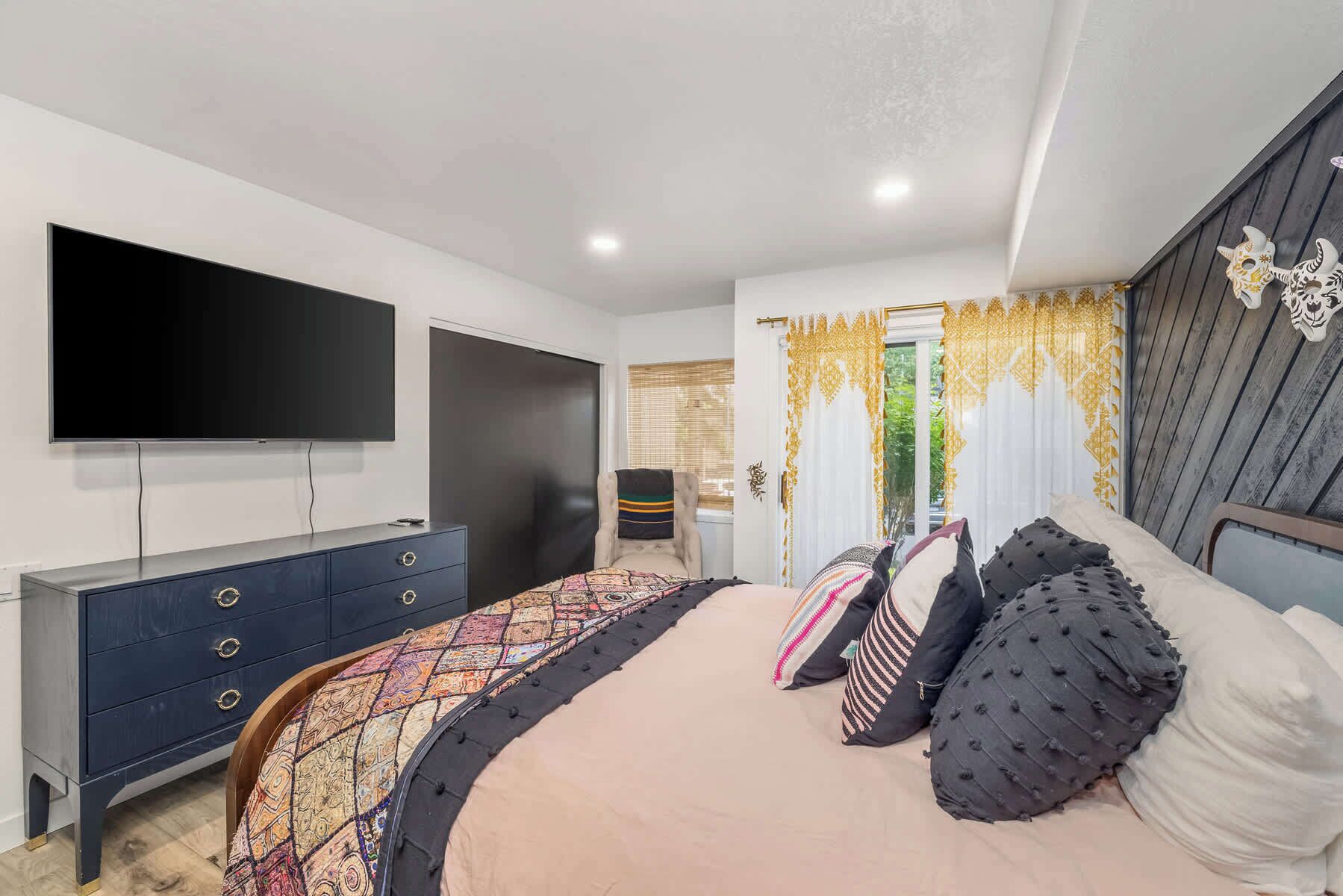 A bedroom with a large bed, a TV, a dark dresser, and a chair.
