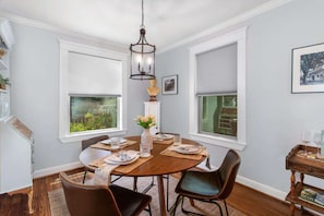 A dining room with a round table, chairs, a vase with flowers, and a chandelier.