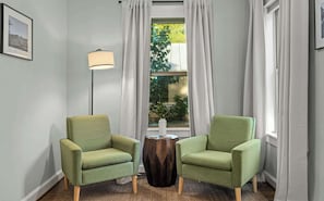 Une piĂšce avec deux fauteuils verts, un lampadaire, une table dâappoint et une fenĂȘtre avec des rideaux.