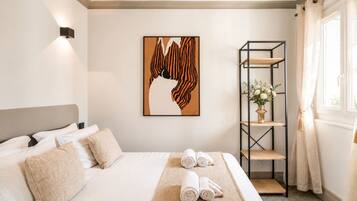 A hotel room with a bed, a wall-mounted artwork, a shelf with flowers, and a window with curtains.