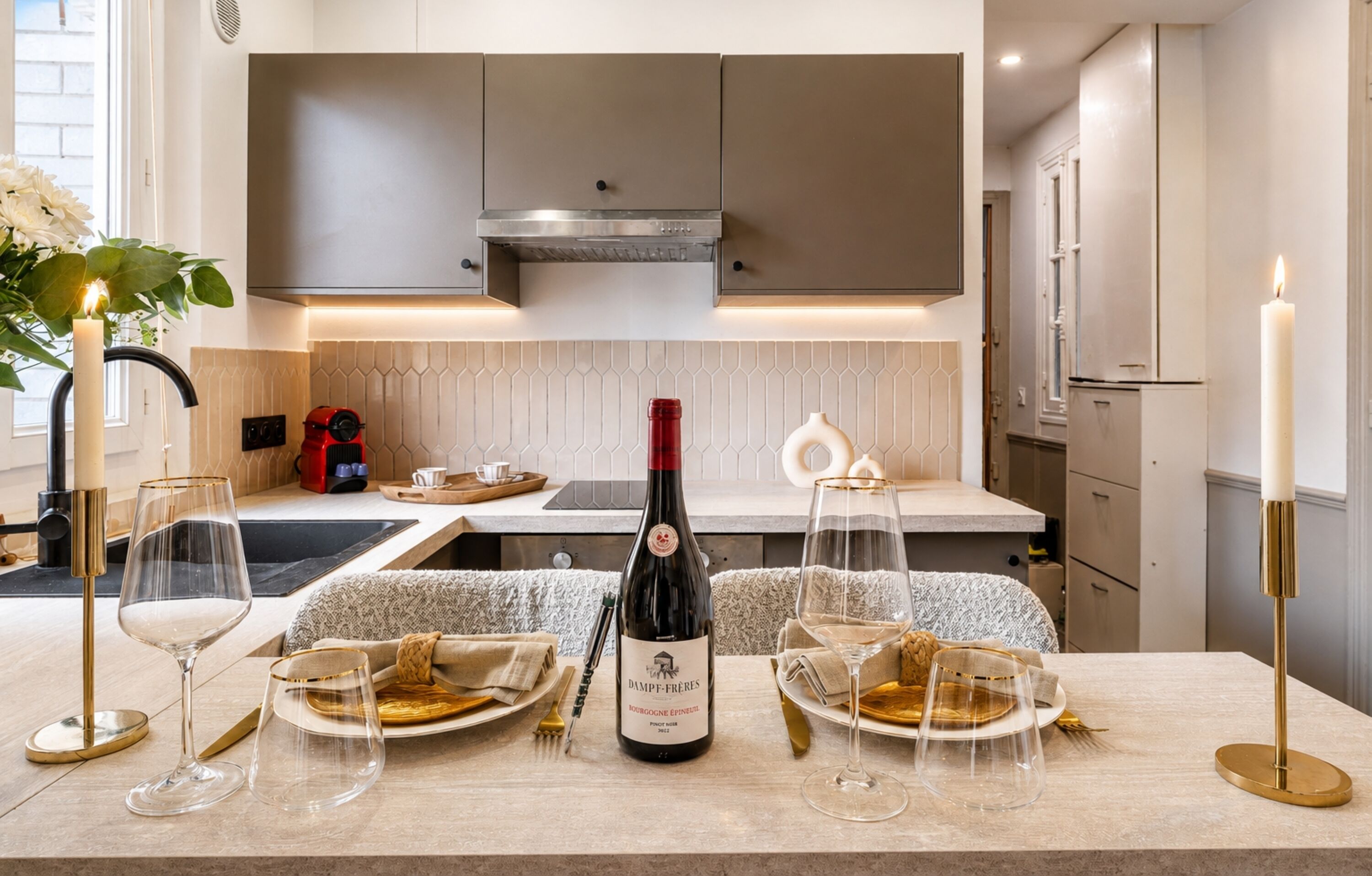 A modern kitchen with a wine bottle, glasses, and a candle on the counter.