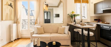 A modern apartment with a living room, kitchen, and dining area. There is a sofa, two round tables, and a kitchen counter with stools.