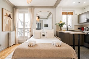 Quarto de hotel moderno com uma cama grande, área de estar, cozinha compacta e vista para a cidade.