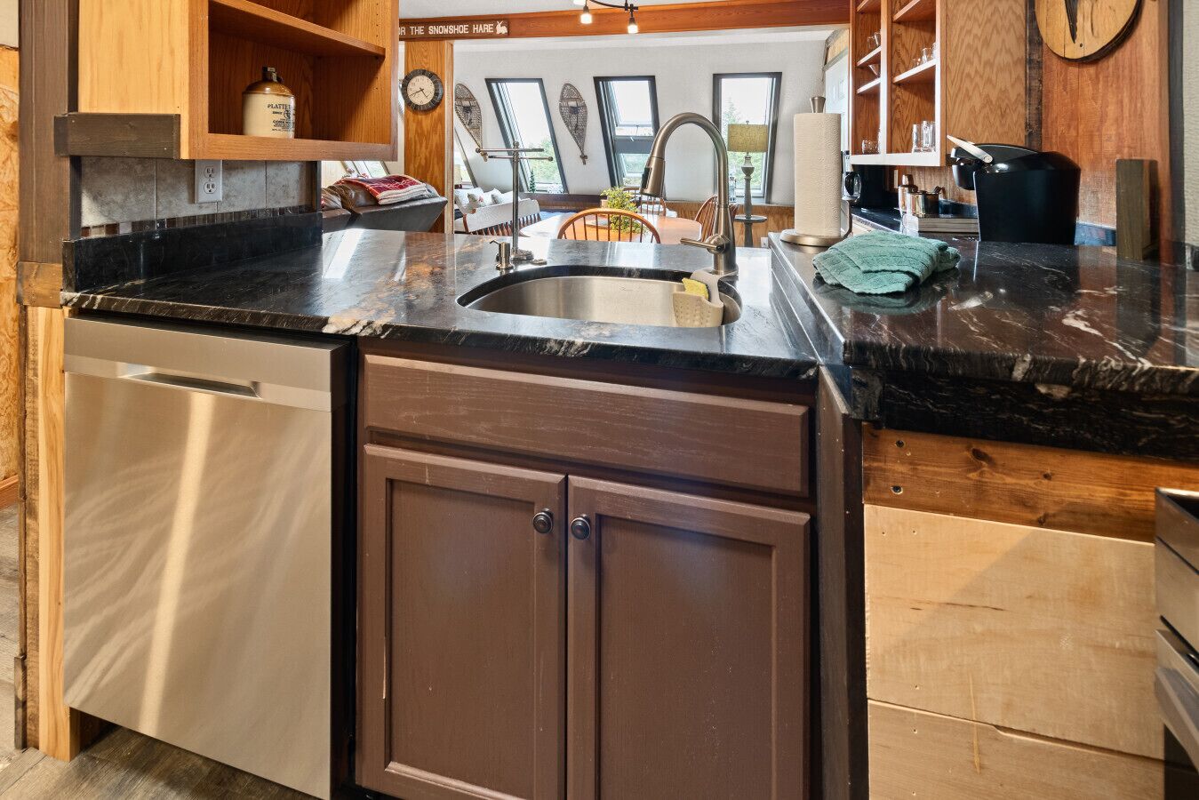 A kitchen with a stainless steel dishwasher, a sink with a faucet, wooden cabinets, and a countertop with a towel.