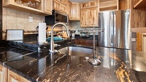 A kitchen with wooden cabinets, a stainless steel refrigerator, a marble countertop, and a built-in sink.