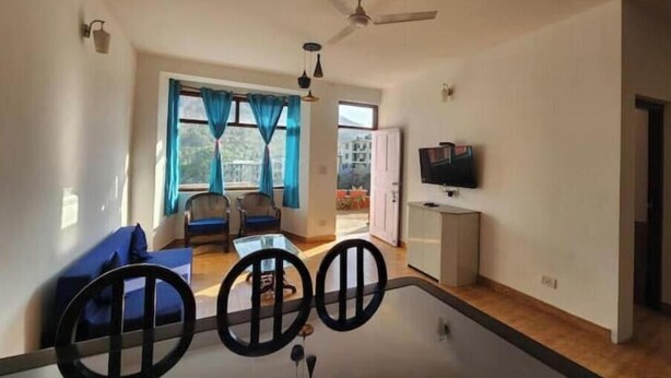 A spacious living room with a large glass coffee table, two armchairs, a ceiling fan, and a TV mounted on the wall. - Villa Kartina 3 BHK near Sattal Lake (Bhowāli)