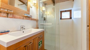 Een badkamer met een houten wastafelmeubel, een glazen douchecabine en een klein raam.