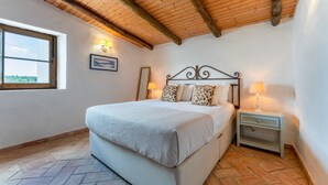 Ein Schlafzimmer mit einem Bett, zwei Nachttischen, einem Fenster und einer Holzbalkendecke.