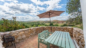 Eine Terrasse mit Steinmauer, Holztisch, Bank, Grill und Sonnenschirm.
