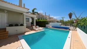 Une piscine avec des chaises longues, un espace abrité et un escalier menant à une porte.