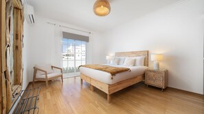 Une chambre à coucher comprenant un lit, une chaise, une table de chevet et une fenêtre donnant sur des immeubles.