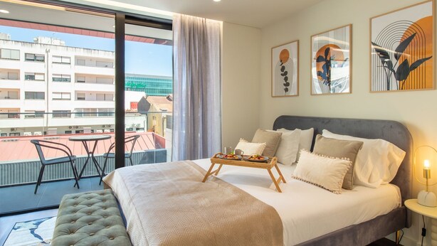 Habitación de hotel con cama, balcón con sillas y obras de arte en las paredes.