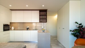 Una cocina moderna con armarios blancos, horno integrado, cafetera y un pequeño estante con adornos.