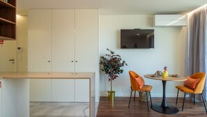 Una habitación de hotel moderna con zona de comedor, televisor montado en la pared y una planta en maceta.